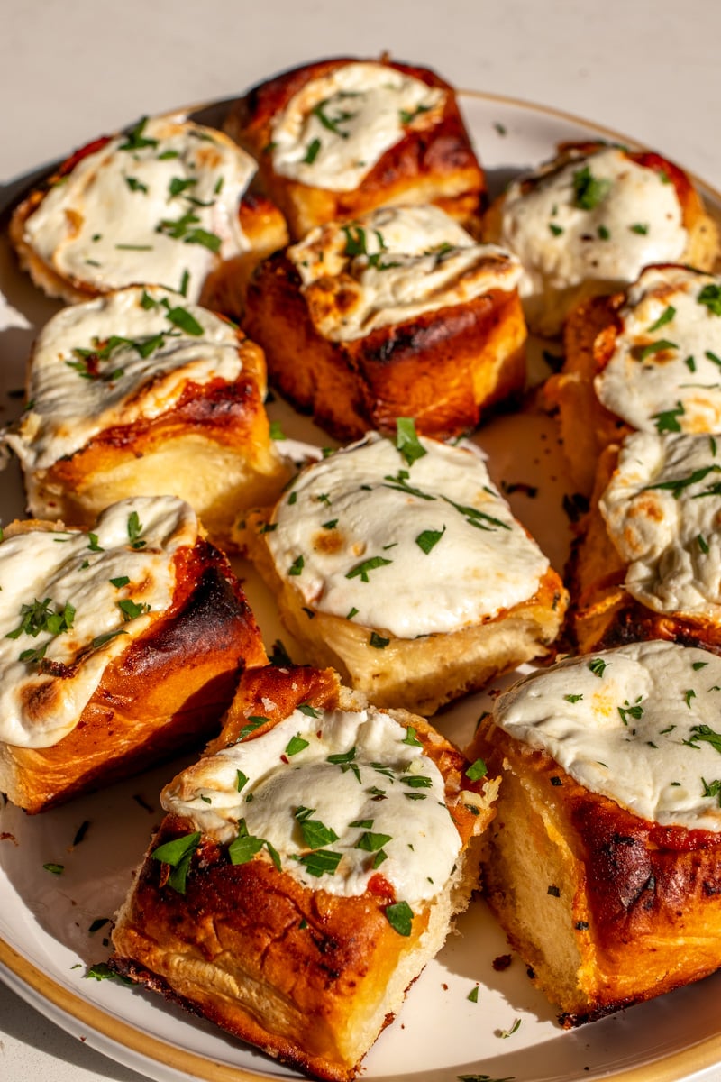 a birds eye view of a white platter topped with a dozen cheesy meatball sliders.