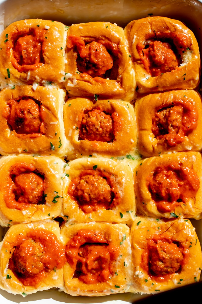 a white baking dish filled with meatball stuffed kings hawaiian rolls.