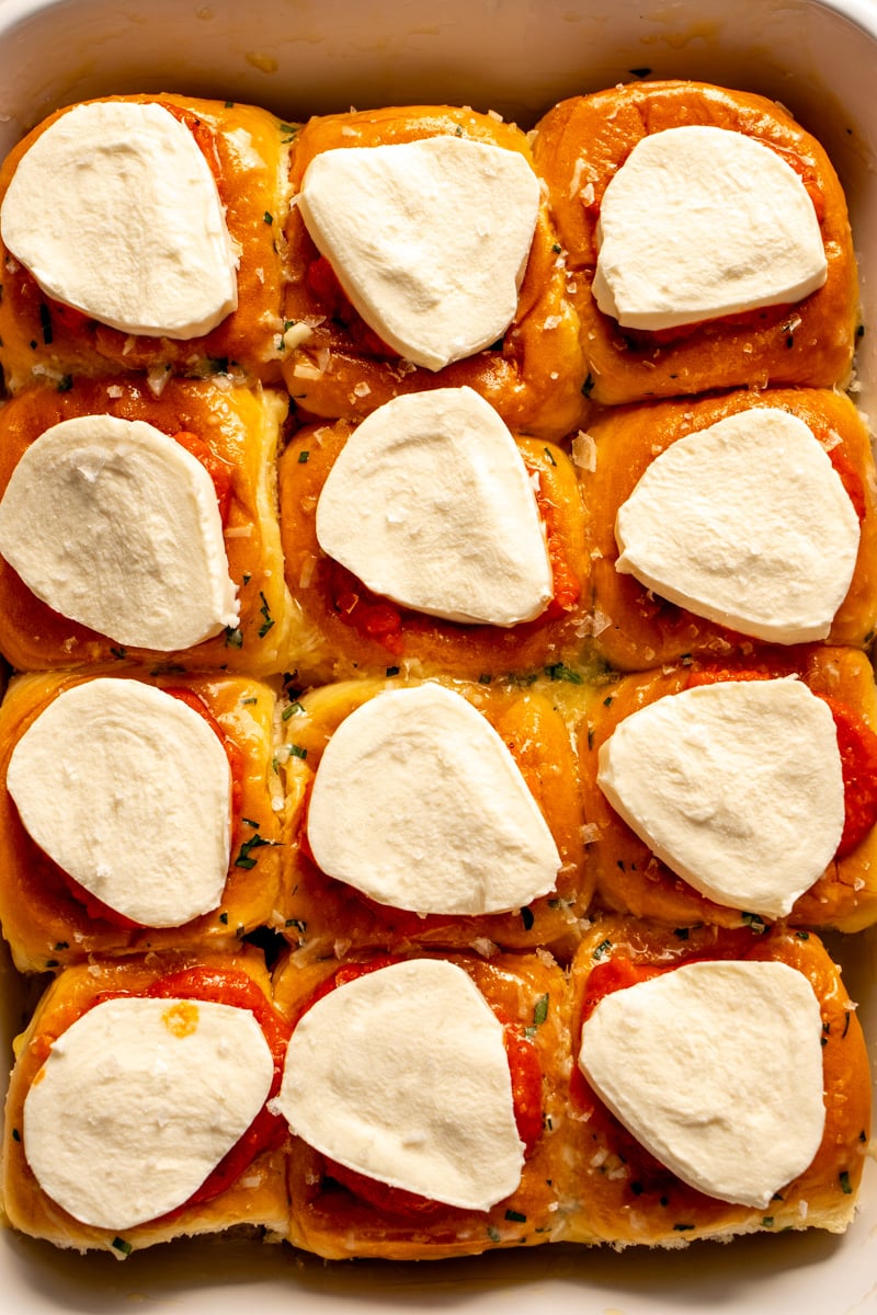 mozzarella topped meatball sliders in a baking dish before going in the oven.