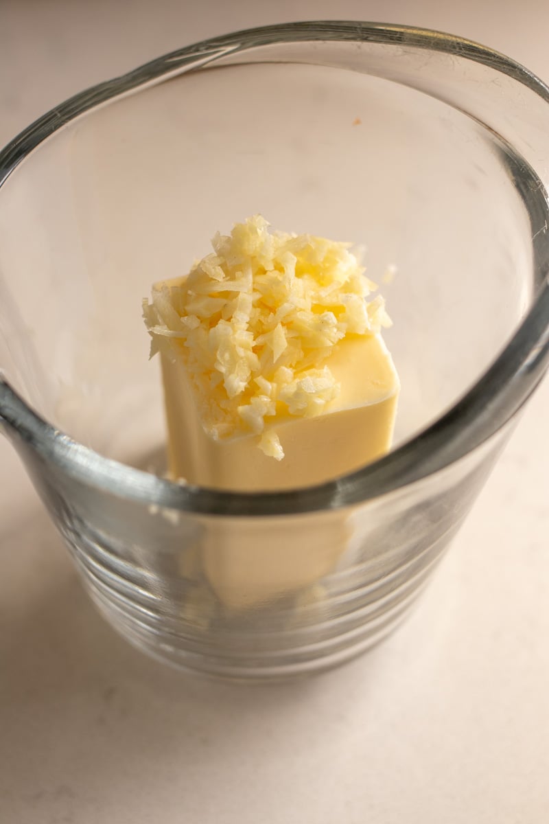 a half stick of butter and chopped garlic in a glass measuring cup.