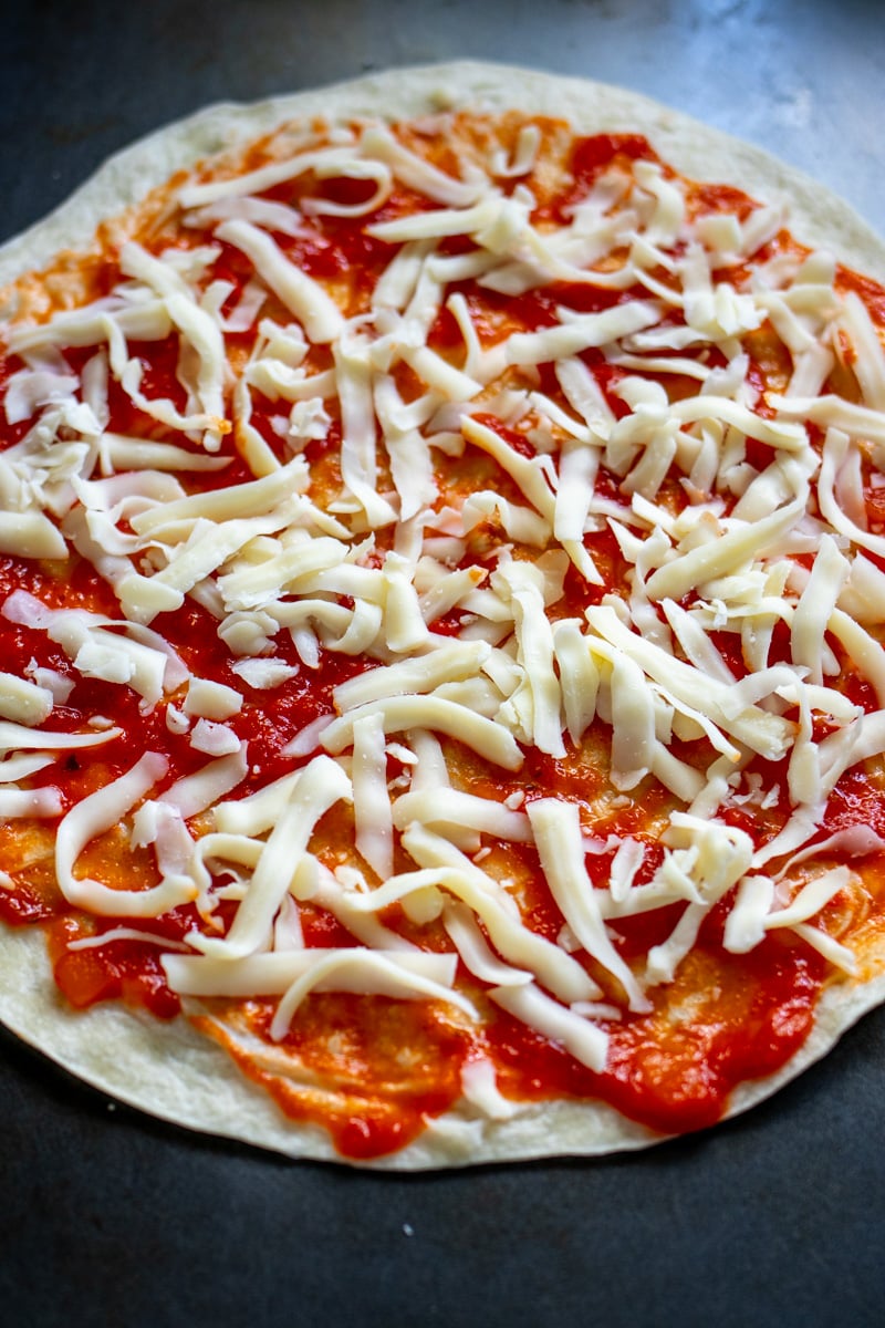 a tortilla topped with marinara sauce and shredded cheese.
