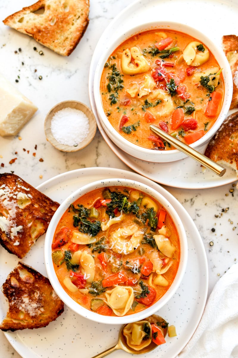 an overhead view of two bowls of vegetarian cheese tortellini soup. 
