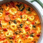 a green pot full of bright orange creamy cheese tortellini soup with lots of veggies.