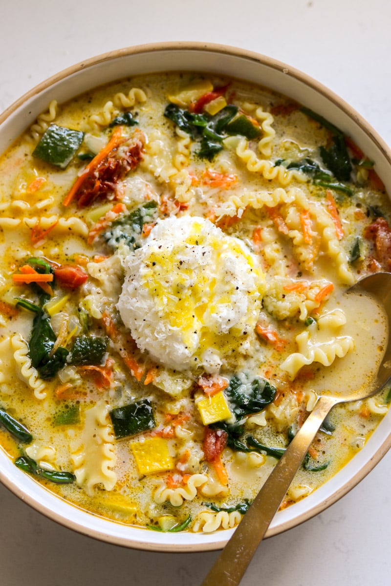 a big white bowl filled with white lasagna soup with colorful veggies and ricotta cheese on top.