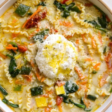 a big white bowl filled with white lasagna soup with colorful veggies and ricotta cheese on top.