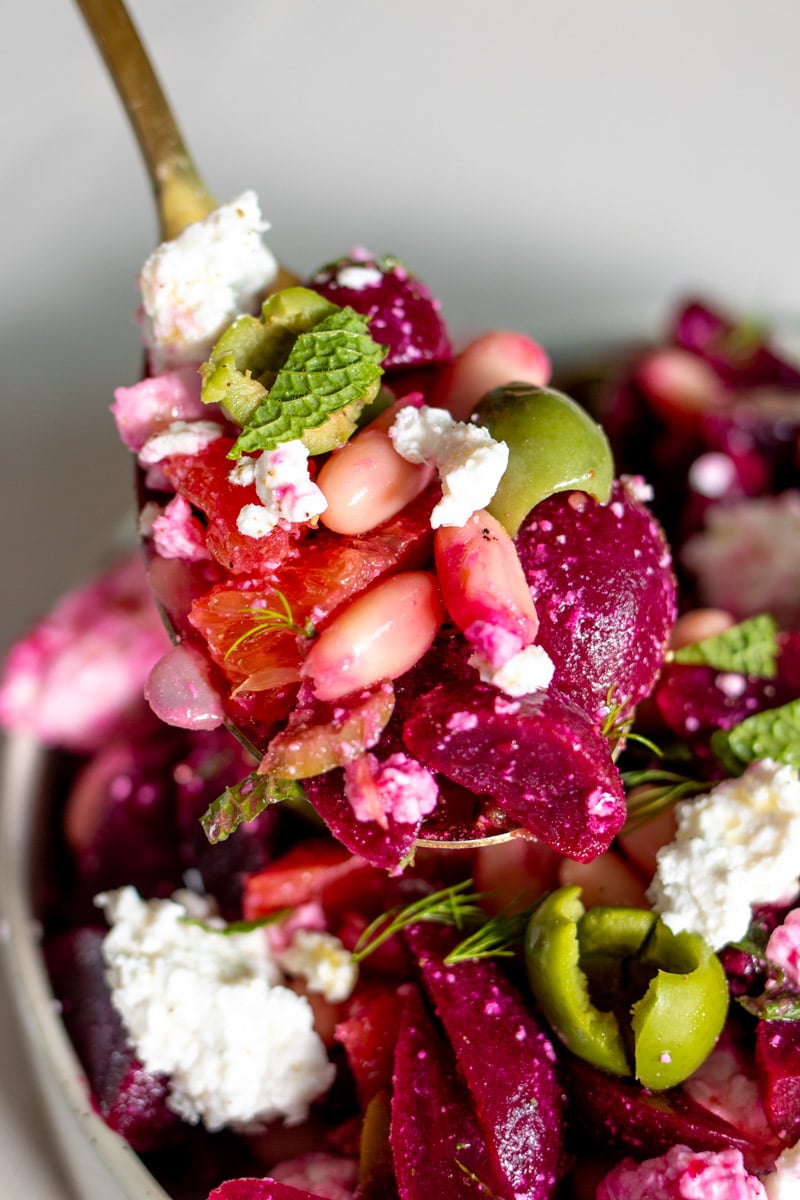 a golden spoon holding a scoop of beet and feta salad.