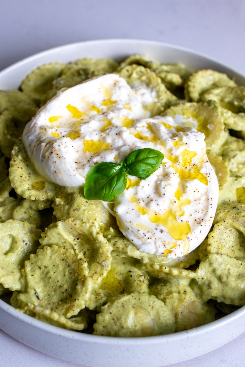 an up close view of a bowl of bright green pesto pasta with broccoli and burrata.