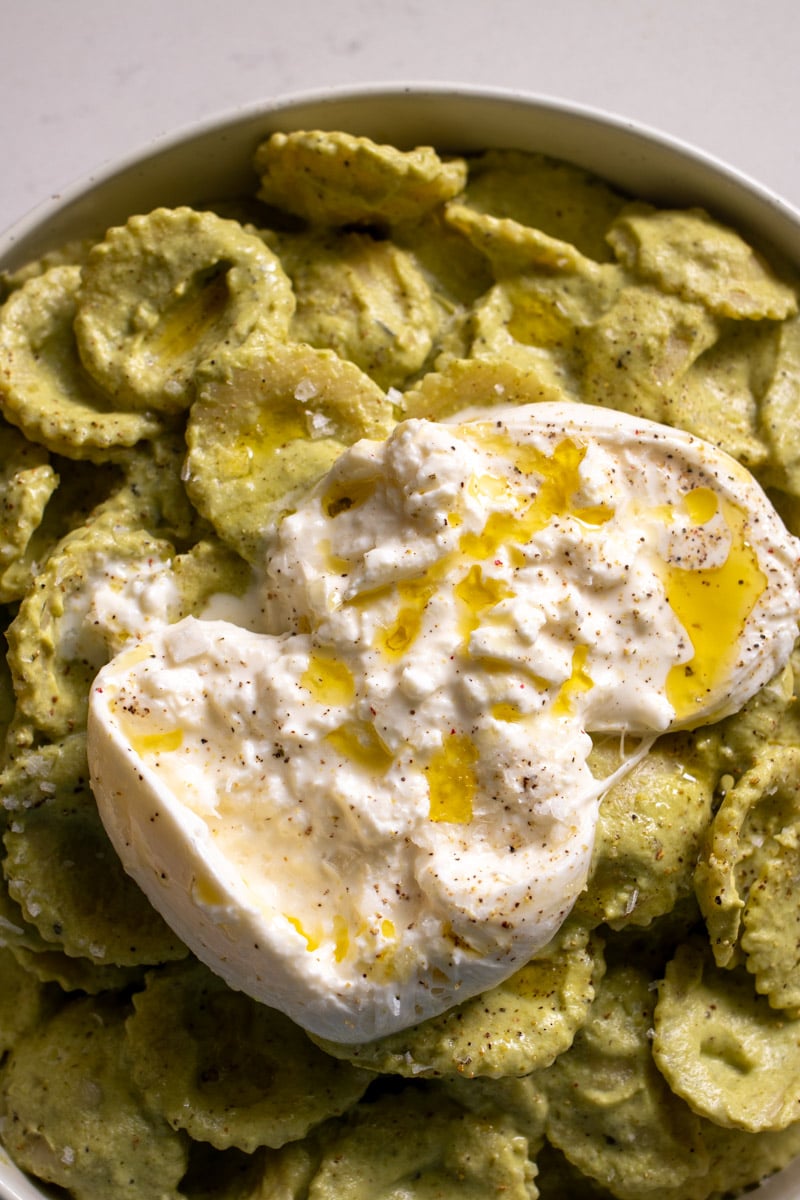 a ball of burrata torn up on top of a bowl of green pasta sauce.