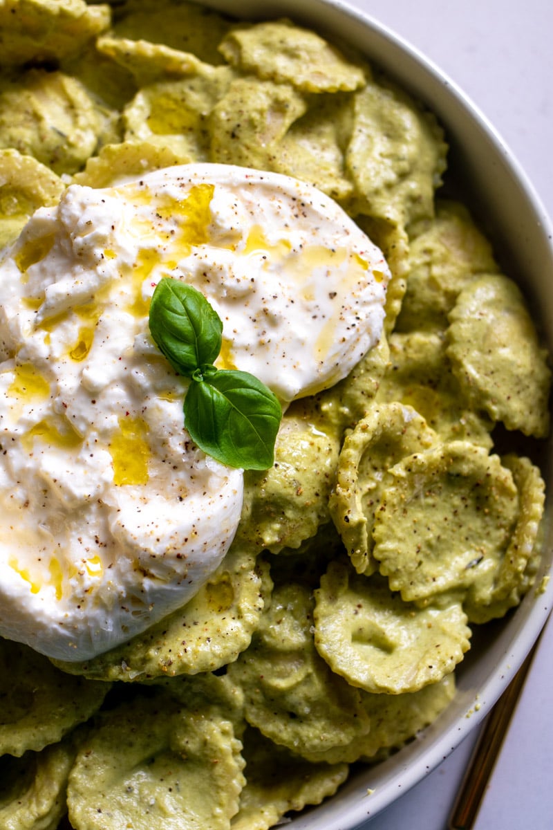 the right side of a bowl of bright green pasta with burrata on top.