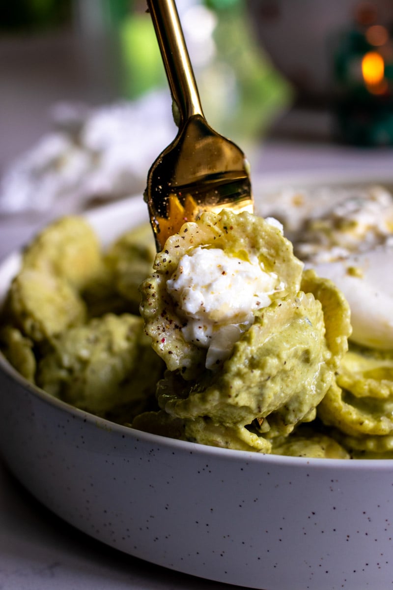 a golden fork holding a scoop green pasta. 