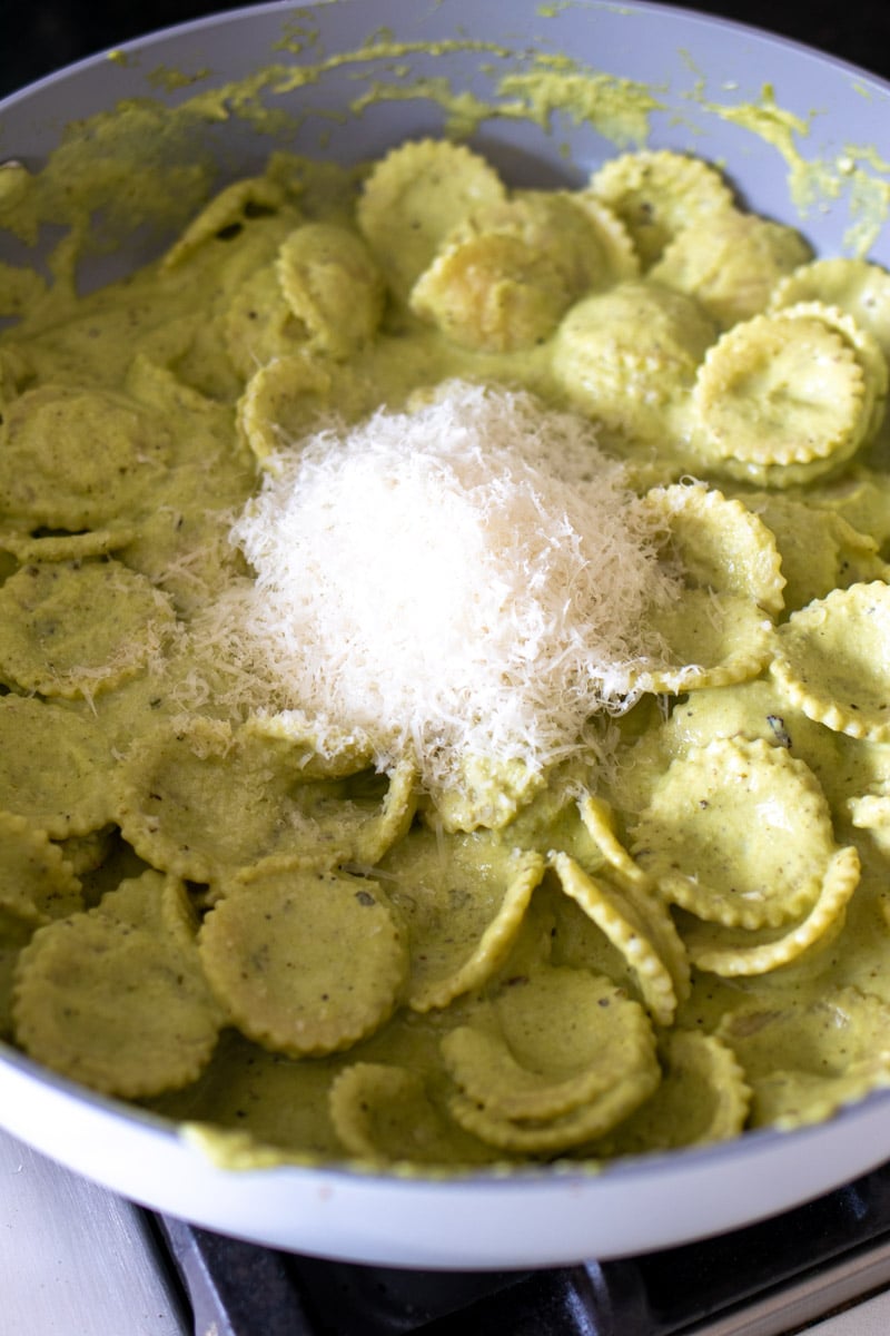 brococli pesto being tossed with pasta with parmesan cheese on top.