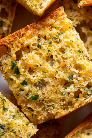 garlic powder garlic bread toast on a white plate -- all stacked on top of each other.