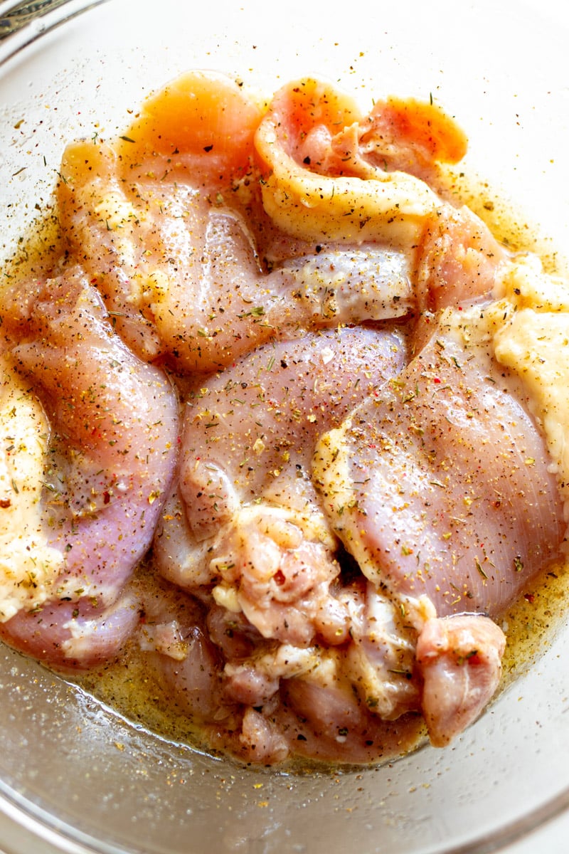 raw chicken marinating in a bowl with spices on top. 