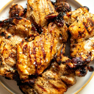 a white plate full of grilled boneless skinless chicken thighs with sear marks.