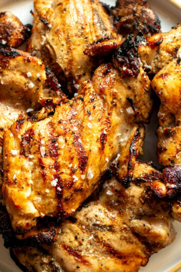 a white plate full of grilled boneless skinless chicken thighs with sear marks.