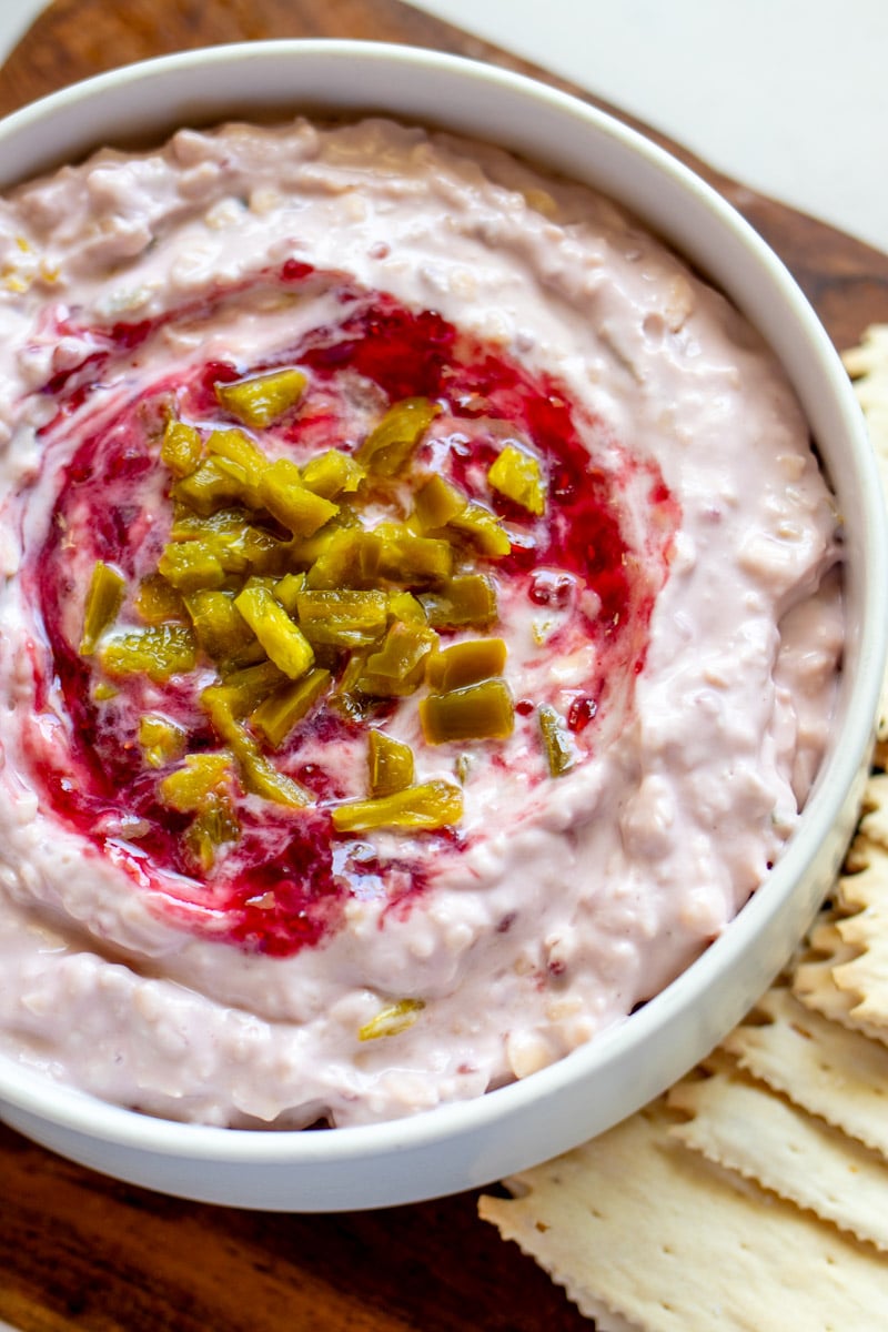 overhead of a white bowl full of pink raspberry jalapeno dip with crackers on the side. 