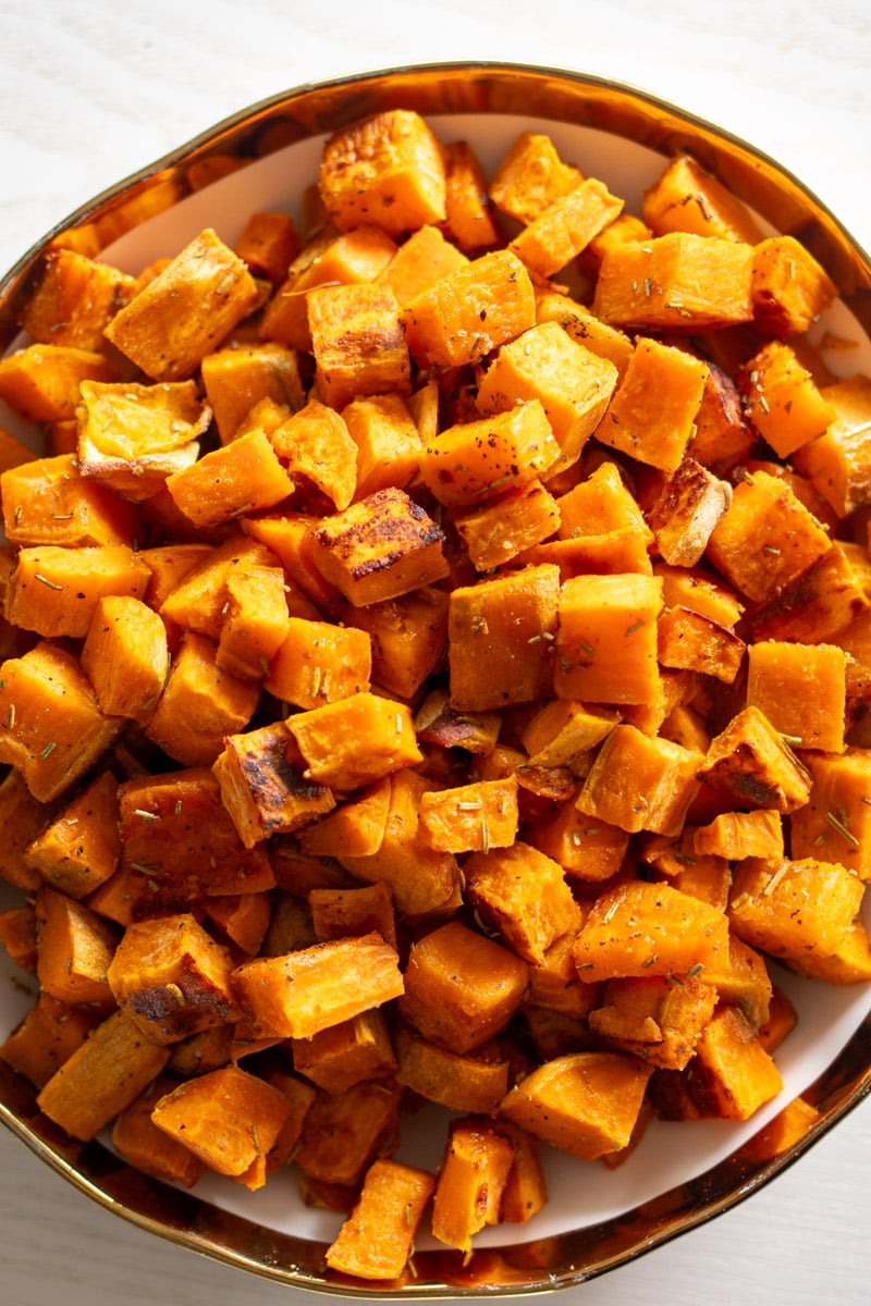 a white bowl with a gold rim filled with tiny caramelized sweet potato cubes.