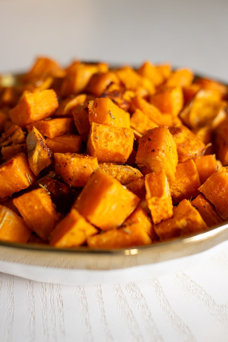 the side of a white bowl filled with bright orange sweet potato cubes.