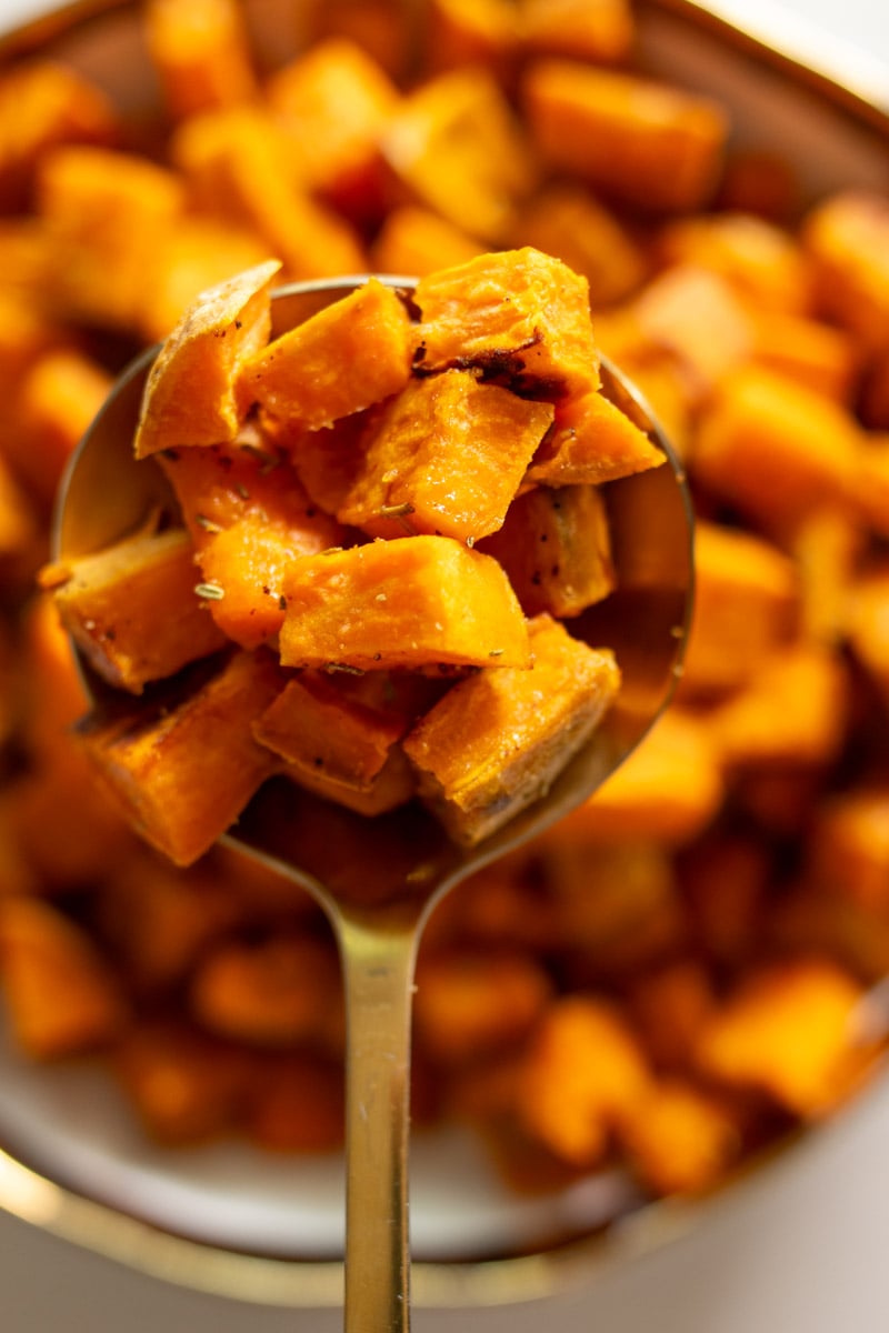 a golden spoon holding a scoop of rosemary roasted sweet potatoes. 