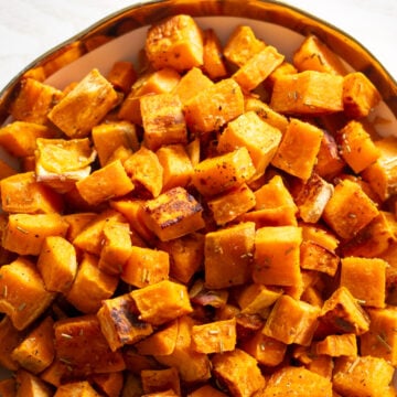 a white bowl with a gold rim filled with tiny caramelized sweet potato cubes.