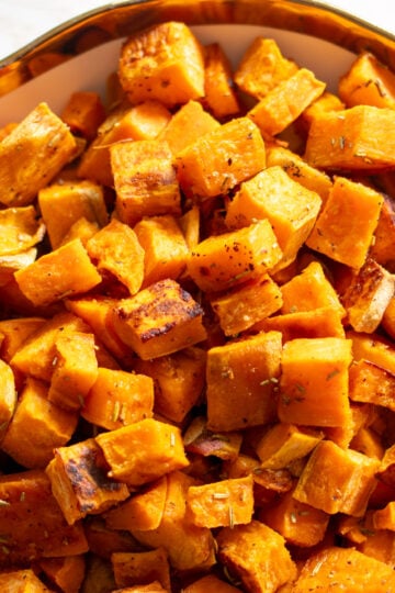 a white bowl with a gold rim filled with tiny caramelized sweet potato cubes.