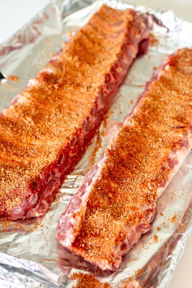 a rack of ribs with rib rub all over them on a large lined baking sheet. 