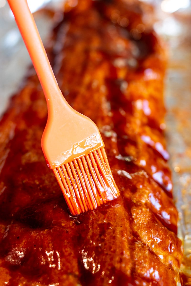 a brush coating bbq sauce onto a rack of ribs. 