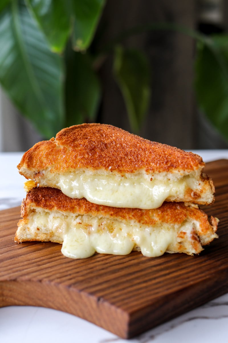 a air fryer grilled cheese cut in half on a cutting board with cheese oozing out the center.