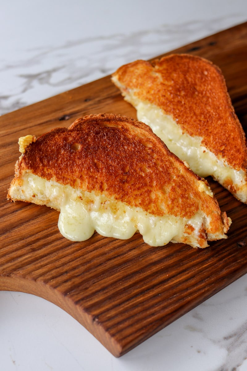 two pieces of an air fryer grilled cheese on a wooden cutting board.