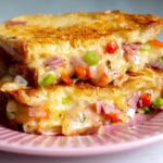 a grinder grilled cheese on a pink plate, split open, with cheese oozing out.