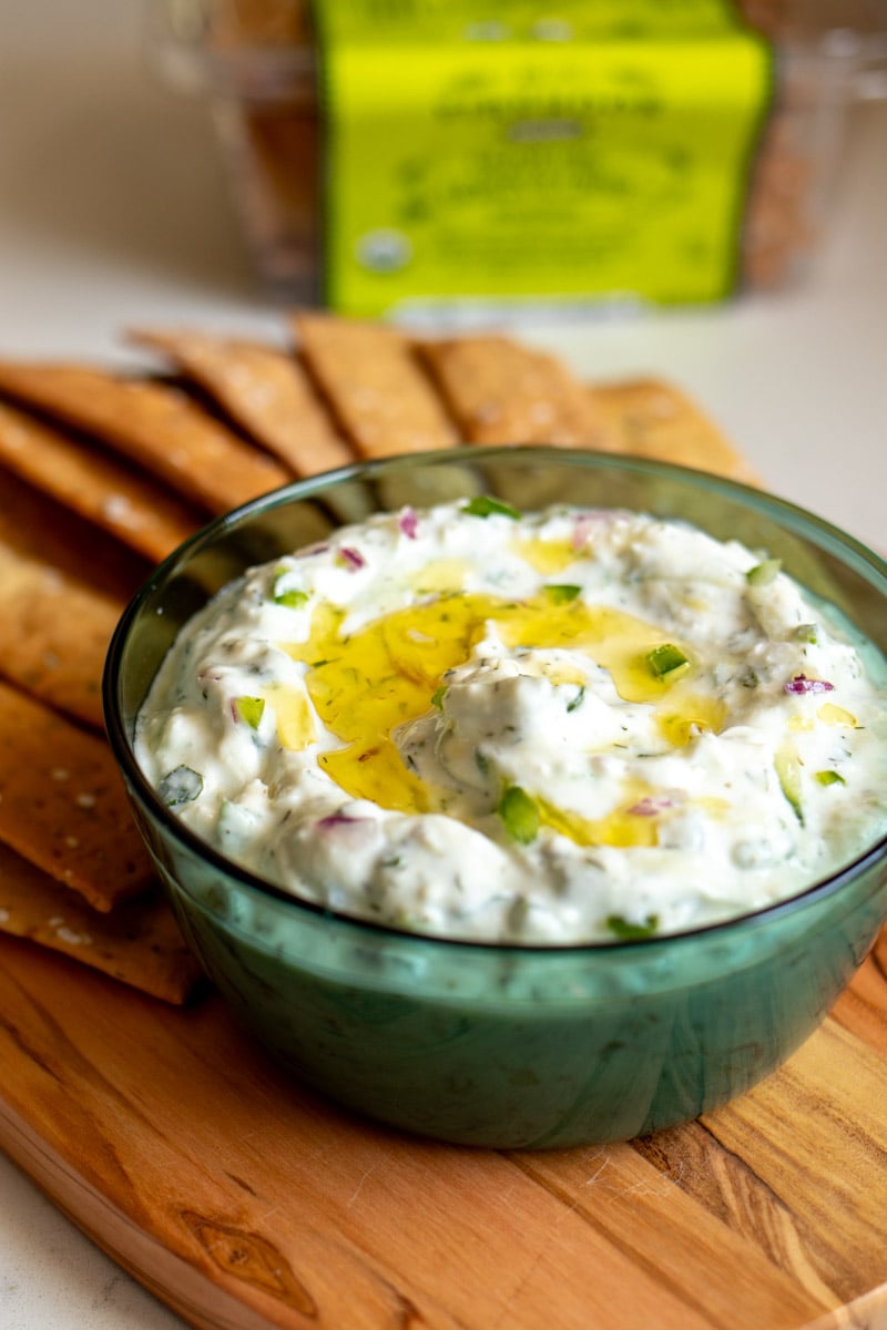a creamy spicy yogurt dip in a green glass bowl with crackers behind it. 
