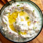 a small green glass bowl filled with a spicy tzatziki dip that's made with jalapenos and feta cheese.