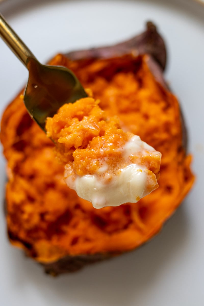 a fork holding a scoop or fluffy sweet potato and butter. 