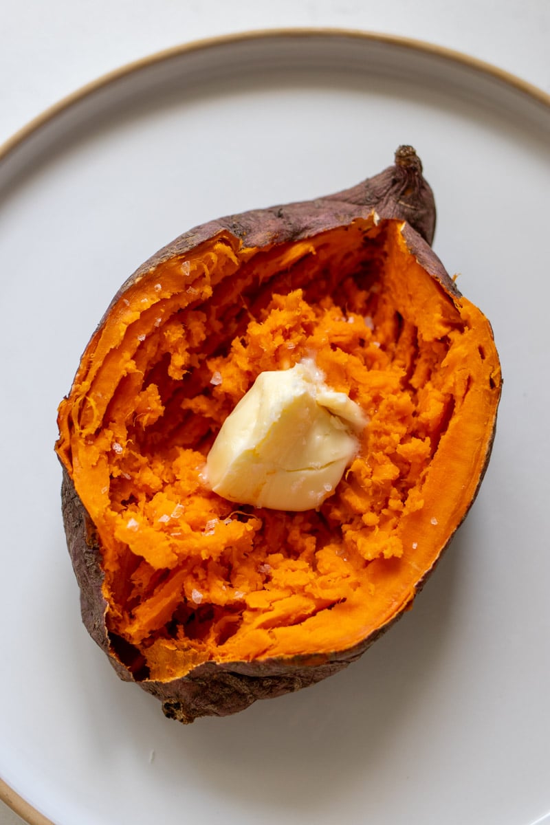 a big fluffy microwave sweet potato split open on a plate with melted butter.