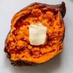 a light and fluffy sweet potato split open with melted butter on a white plate.
