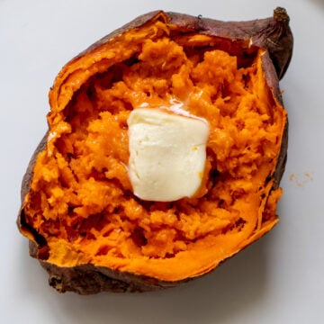 a light and fluffy sweet potato split open with melted butter on a white plate.