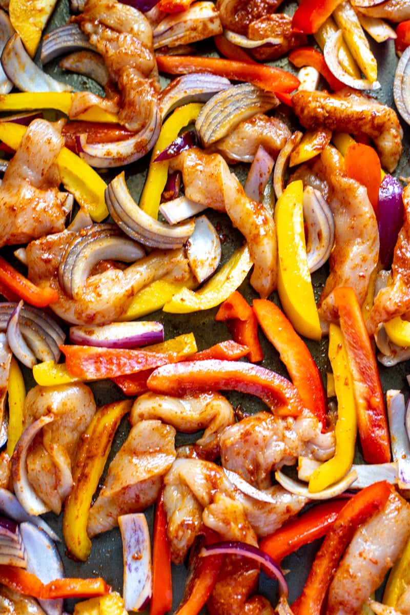 raw chicken with peppers, onions and taco seasoning on a sheet pan.
