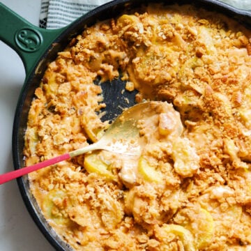 a cast iron skillet full of southern squash casserole with sour cream and ritz crackers.