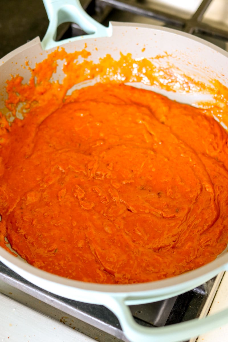 a golden orange spicy vodka sauce in a blue our place pan on the stovetop.