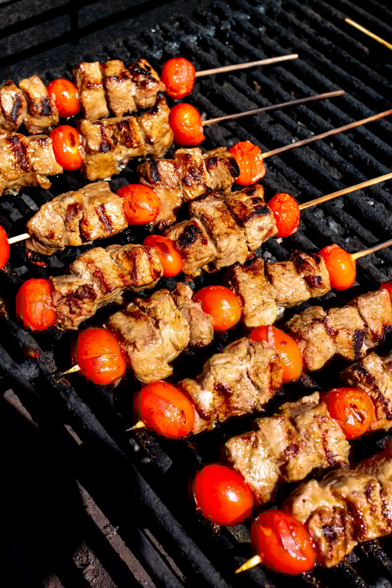 petite sirloin steak skewers with tomatoes on a hot grill.