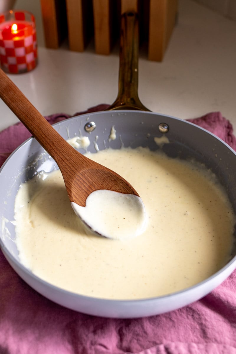 a small white pan filled with white cream sauce with a wooden spoon in it.