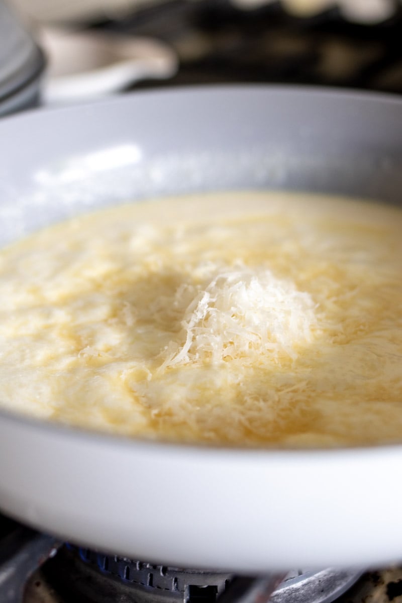 grated parmesan cheese on top of some cream sauce in a skillet.