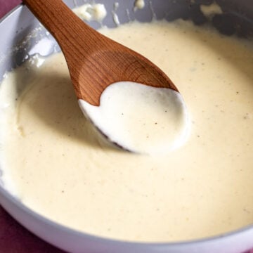 cream sauce in a skillet with a dark wooden spoon scooping out a little bit.