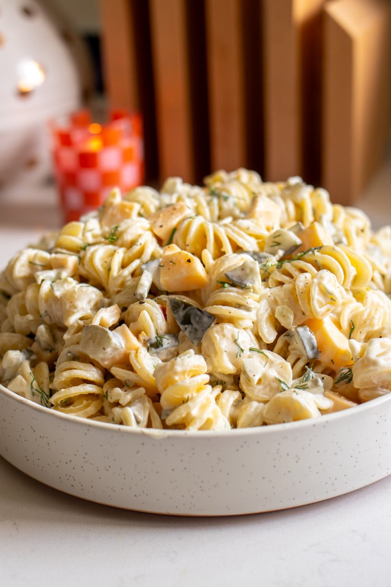 a white bowl filled with a creamy dill pickle pasta salad on a white counter.
