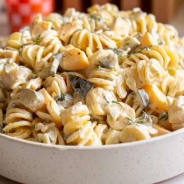 a white bowl filled with a creamy dill pickle pasta salad on a white counter.