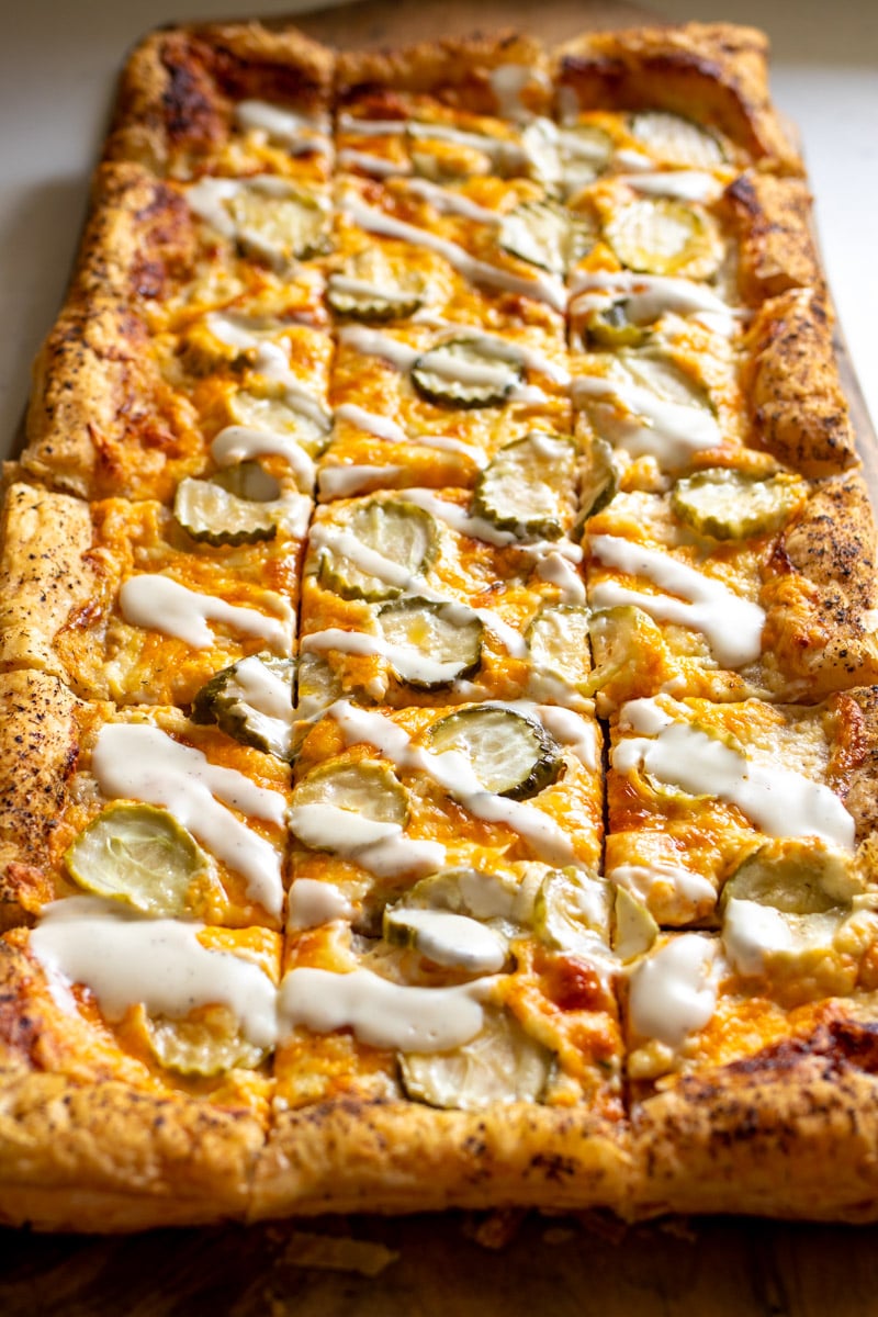 a dill pickle pizza made on a puff pastry with a ranch drizzle.