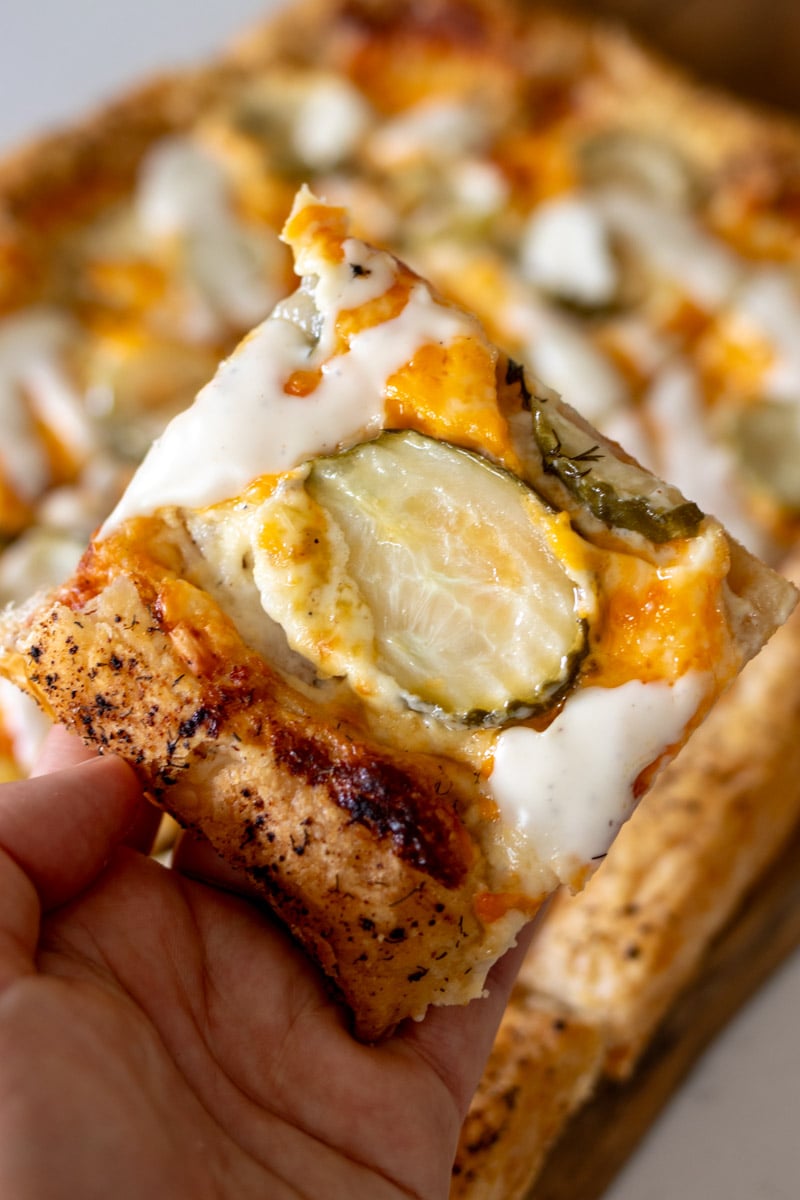 a hand holding a slice of dill pickle pizza. 