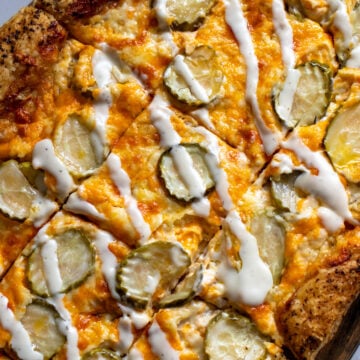 dill pickle pizza drizzled with ranch dressing on a white countertop.