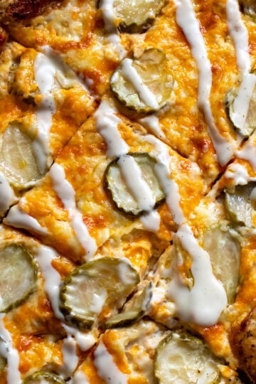 dill pickle pizza drizzled with ranch dressing on a white countertop.