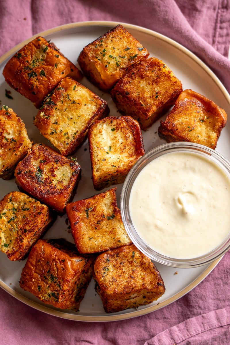 hawaiian roll garlic bread bites on a white plate with alfredo sauce in a clear bowl.